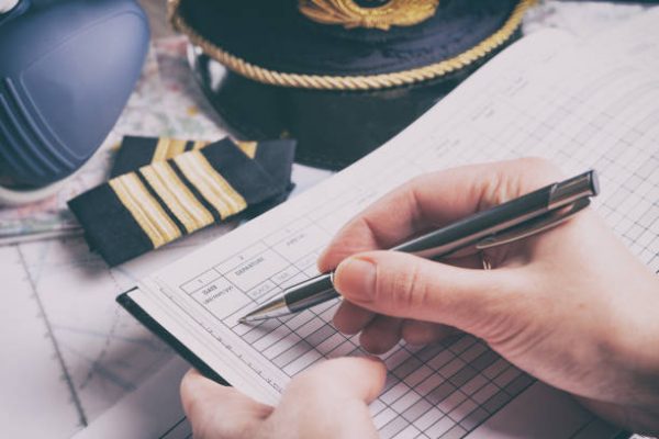 pilot-612×612 Close up of an airplane pilot hand filling in an pre-fligh checklist and holding weather forecast with equipment including hat, epaulettes and other documents in background